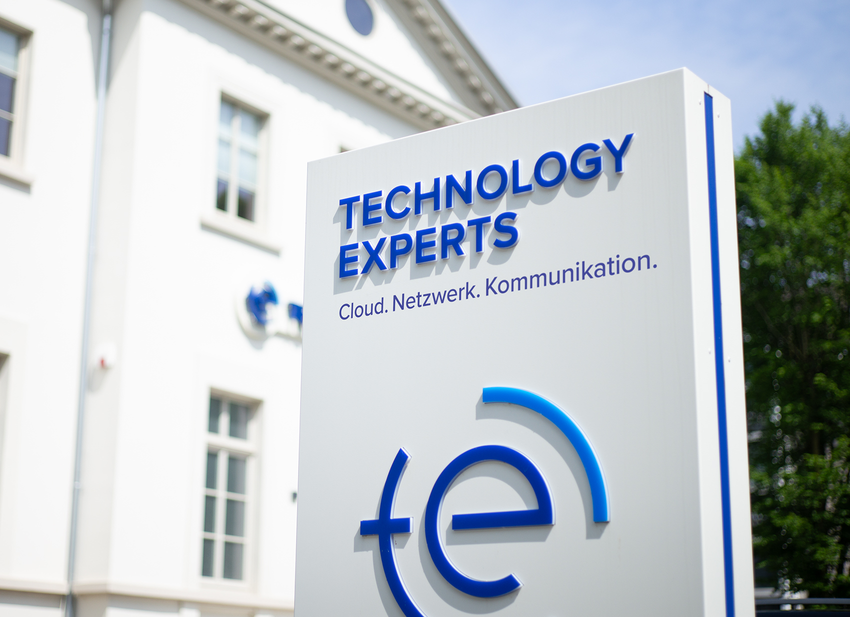 Schild vor Bürogebäude mit Schriftzug: technology experts – Cloud. Netzwerk. Kommunikation.
